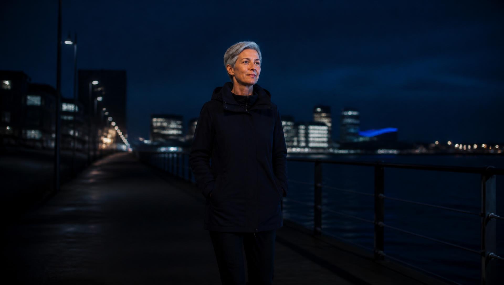 Frau um die 50 bei einem ruhigen Spaziergang an einer Uferpromenade in der Abenddämmerung