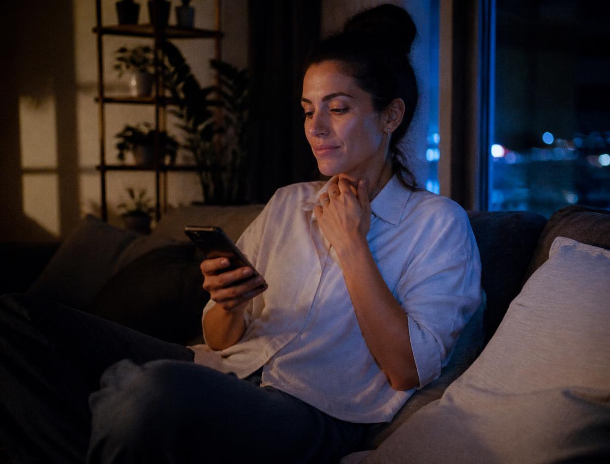 Frau nutzt am Abend entspannt ihr Smartphone auf dem Sofa